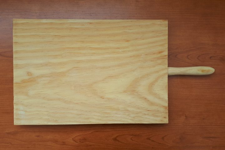 Een lege houten snijplank met steel op een houten ondergrond